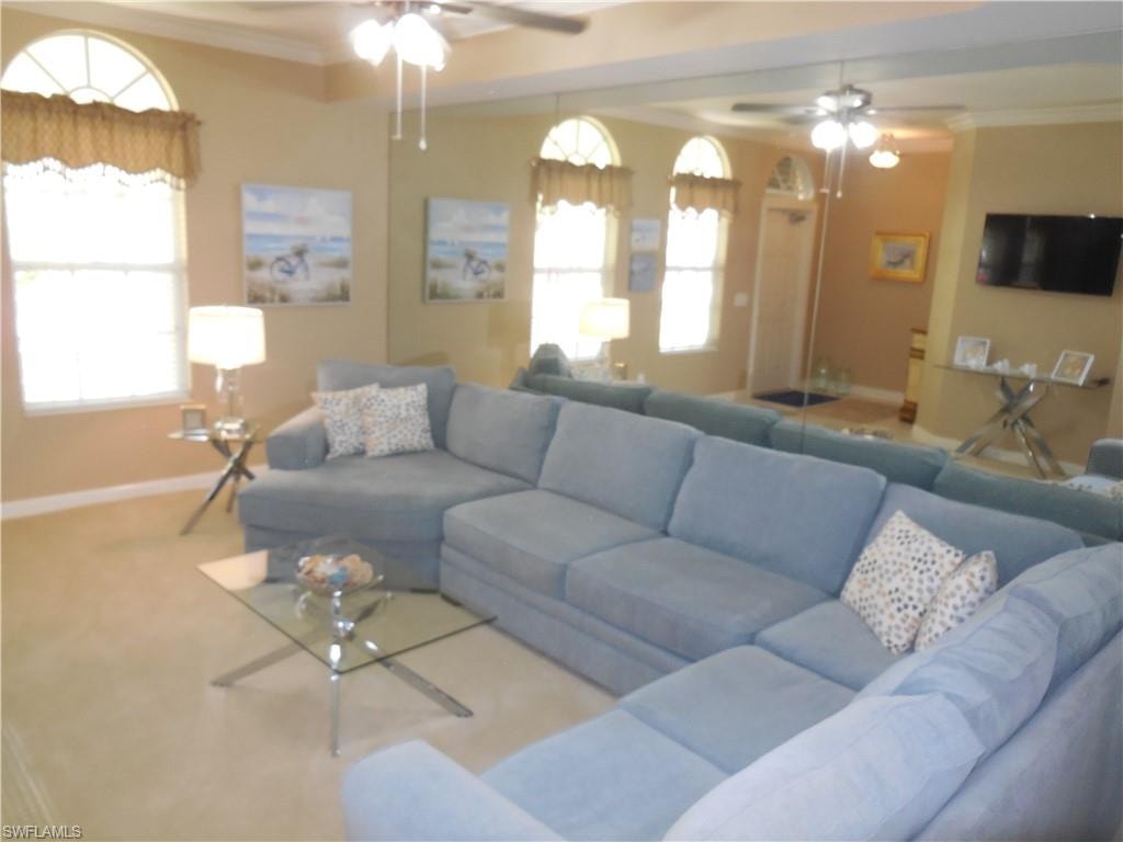 Living area with ceiling fan, baseboards, crown molding, healthy amount of natural light, and carpet flooring