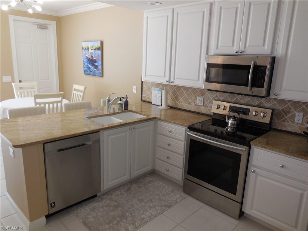 Kitchen featuring stainless steel appliances, a sink, a peninsula, ornamental molding, and tasteful backsplash