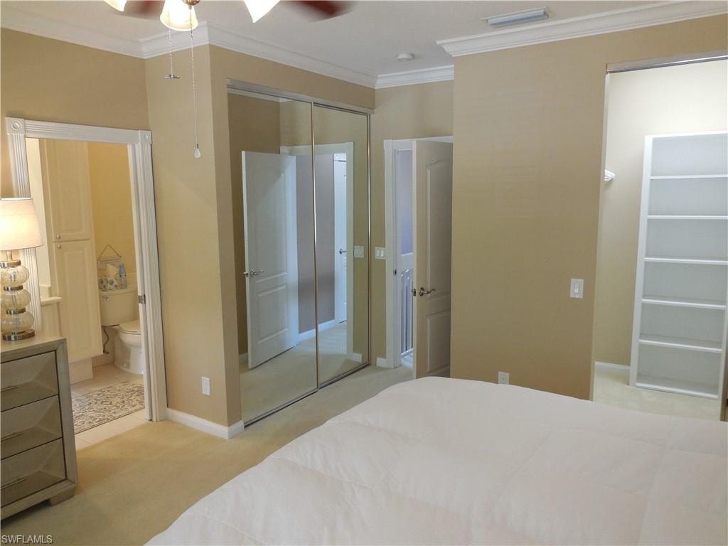 Bedroom featuring crown molding, light carpet, ensuite bath, a closet, and a ceiling fan