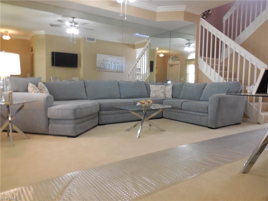 Carpeted living room with stairs, a ceiling fan, crown molding, and healthy amount of natural light
