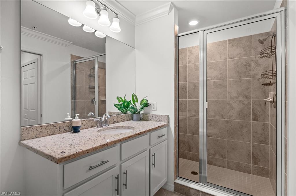 Bathroom featuring a spacious walk-in shower with tile surround, a single vanity with stone countertop, and a large mirror