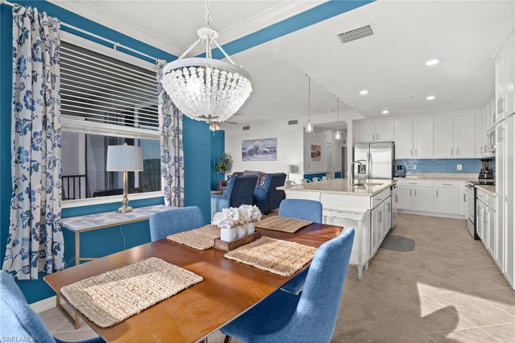 Open-concept kitchen and dining area featuring a crystal chandelier, white cabinetry, stainless steel appliances, and a kitchen island with seating