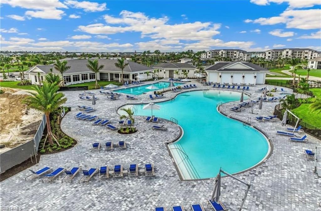 Resort-style pool area featuring multiple swimming pools with integrated steps, expansive paver decking, and surrounding amenity buildings