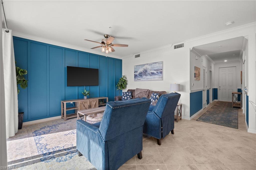 Living area featuring a floor-to-ceiling accent wall with vertical paneling, crown molding, and neutral tile flooring