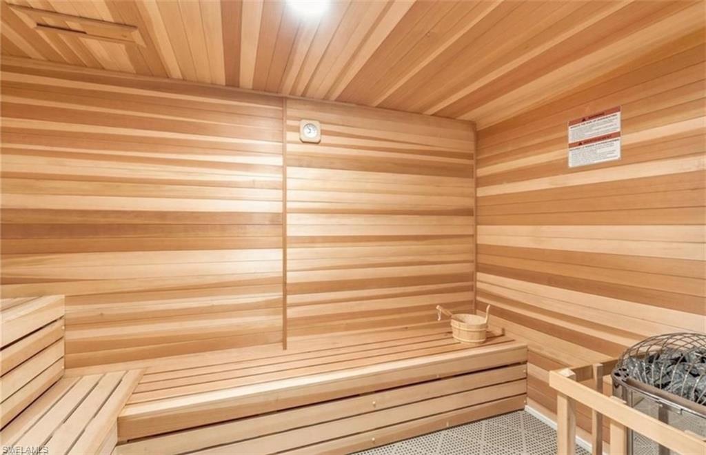 Interior sauna featuring horizontal wood paneling, slatted wood benches, a built-in heater with rocks, and white geometric floor tiles