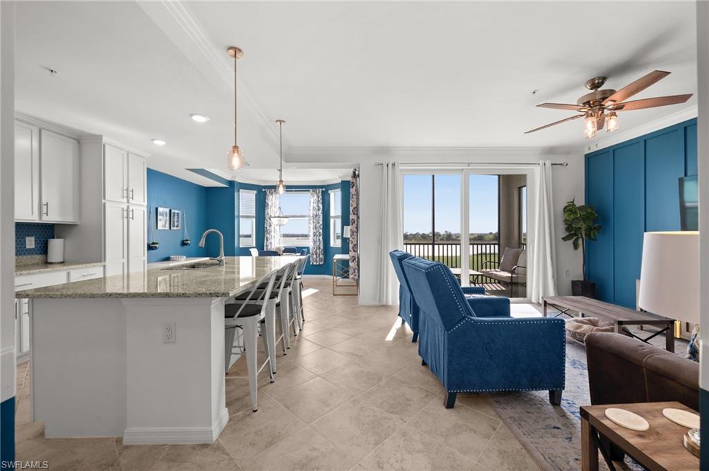 Open-concept living space featuring a kitchen with white cabinetry and a large island, a dining area with bay windows, and a living room with a decorative accent wall