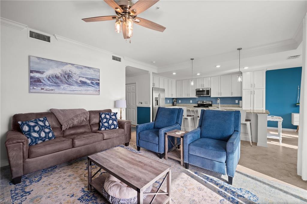 Open-concept living space featuring a ceiling fan, crown molding, light wood-finish flooring, a kitchen island with pendant lighting, and white cabinetry