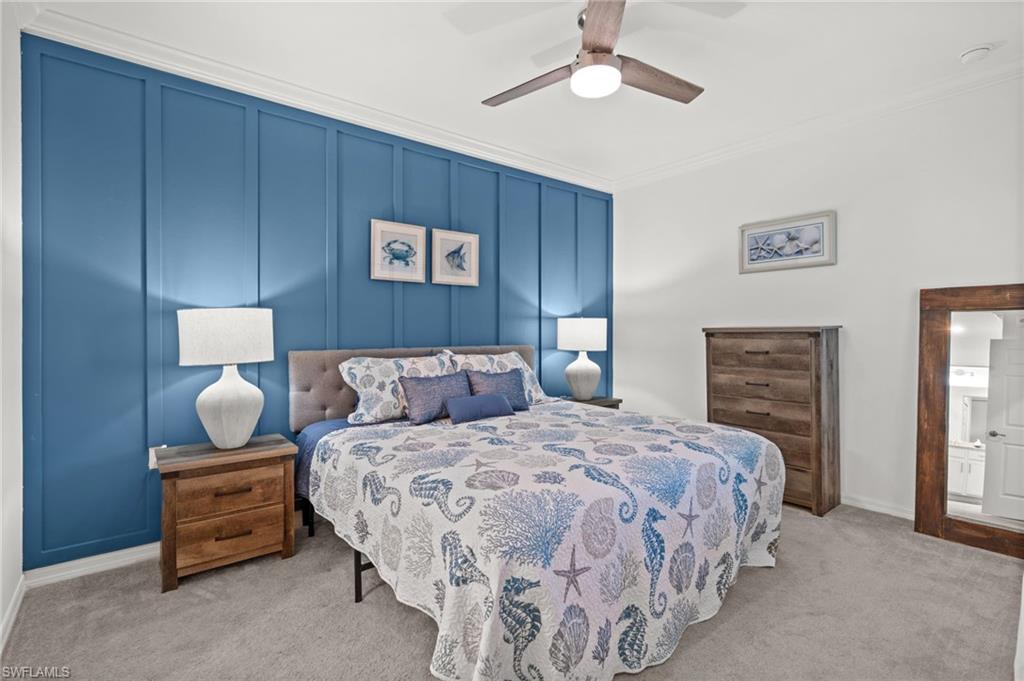 Accent wall with vertical paneling, crown molding, light gray carpet flooring, ceiling fan with integrated lighting, and white baseboards