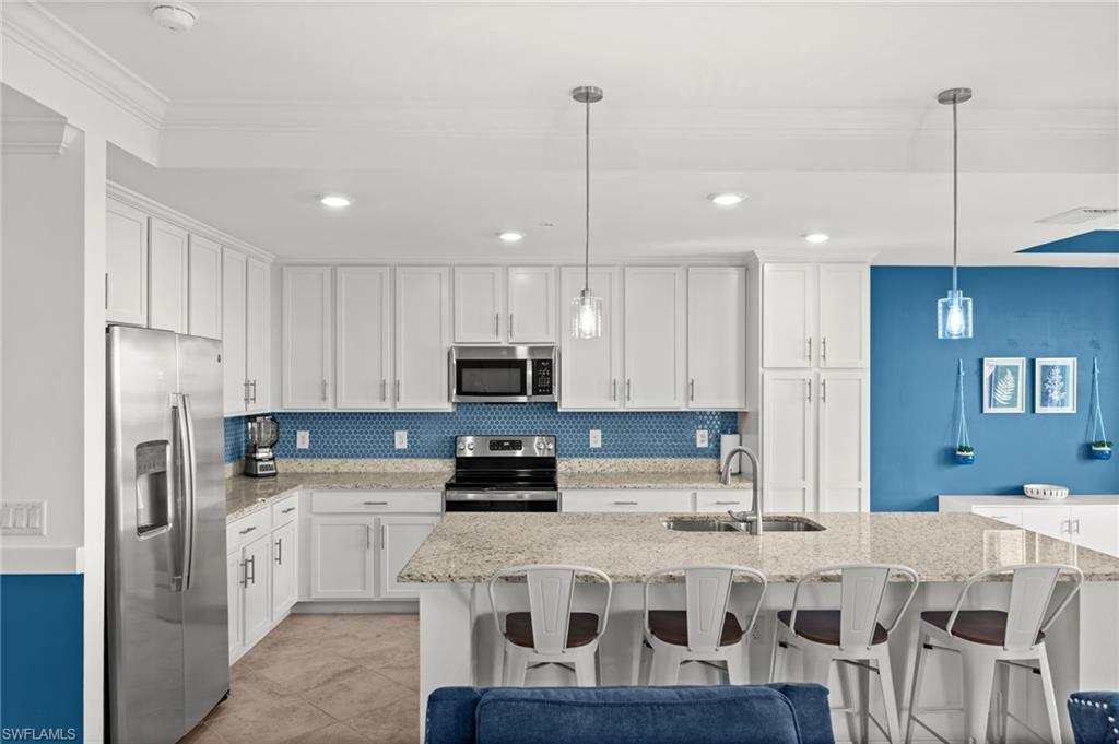 Contemporary kitchen featuring a spacious island with seating, white shaker cabinetry, stainless steel appliances, a blue geometric tile backsplash, and recessed lighting
