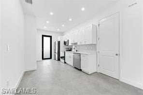 Kitchen #1 featuring stainless steel dishwasher, white cabinetry, light countertops, recessed lighting, and concrete flooring