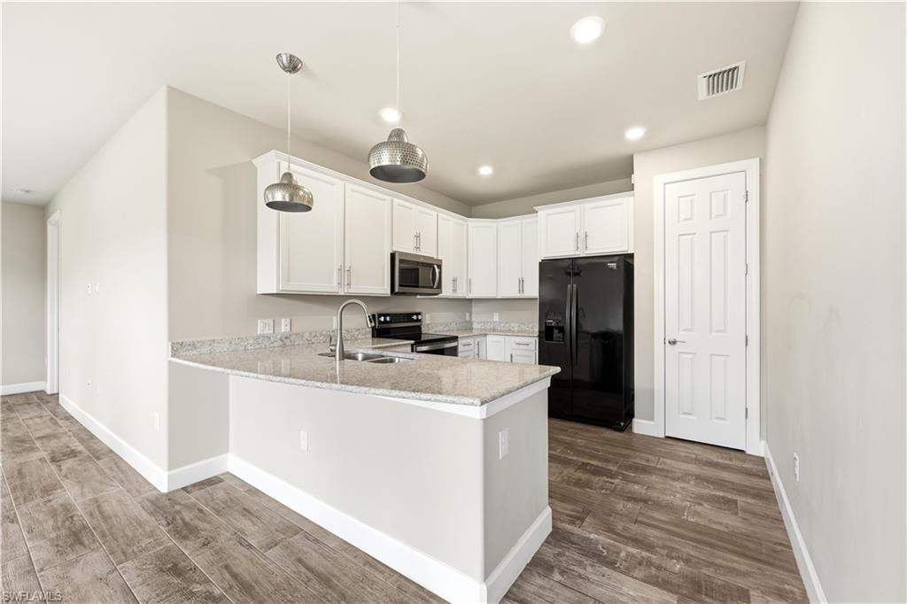 Modern kitchen featuring granite countertops, white cabinetry, a full suite of black appliances, wood-finish flooring, and recessed lighting