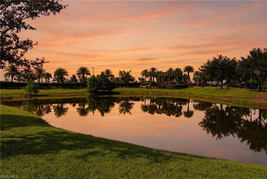 Lush green lawn surrounding a tranquil pond with reflections of various trees and palm trees