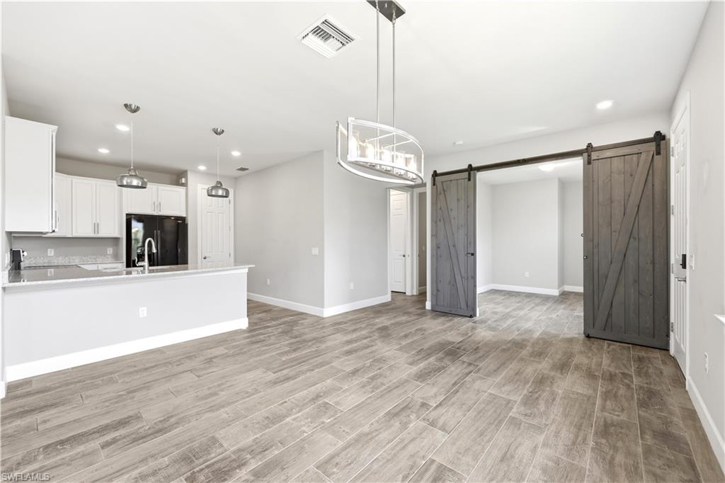 Open-concept living space featuring wood-finish flooring, a kitchen with white cabinetry and dark countertops, recessed lighting, and a contemporary chandelier