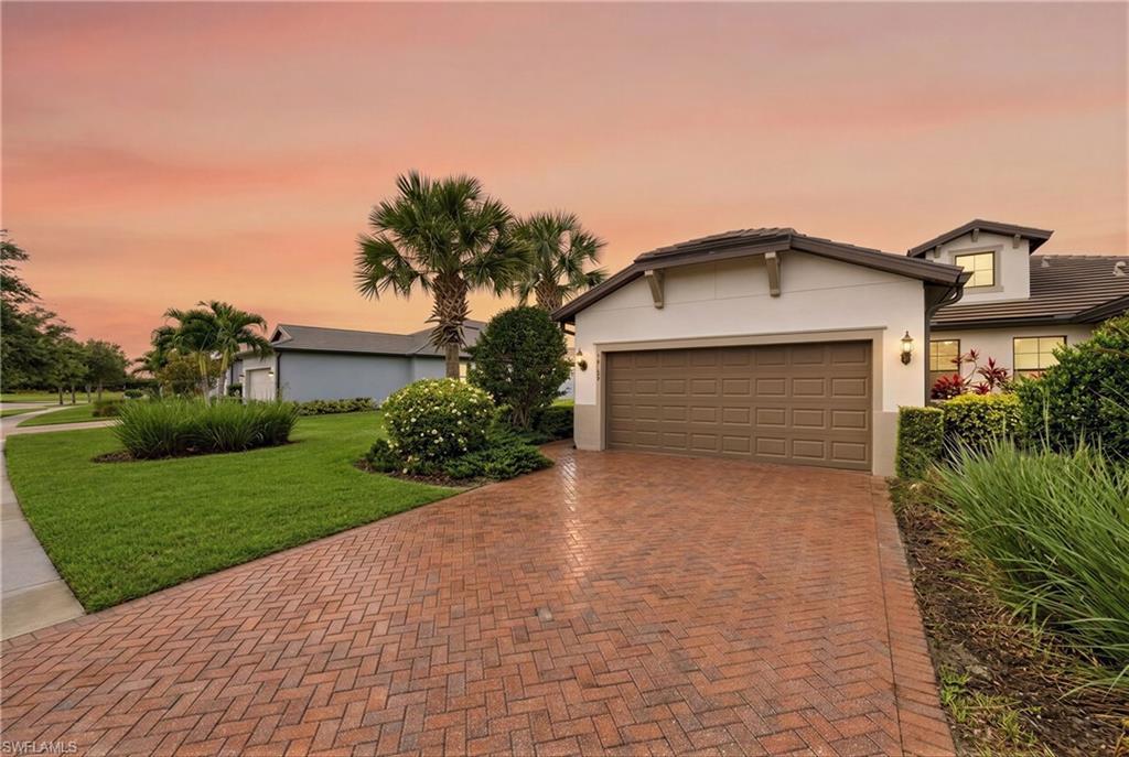 White stucco exterior with a brown garage door, featuring a herringbone brick paver driveway