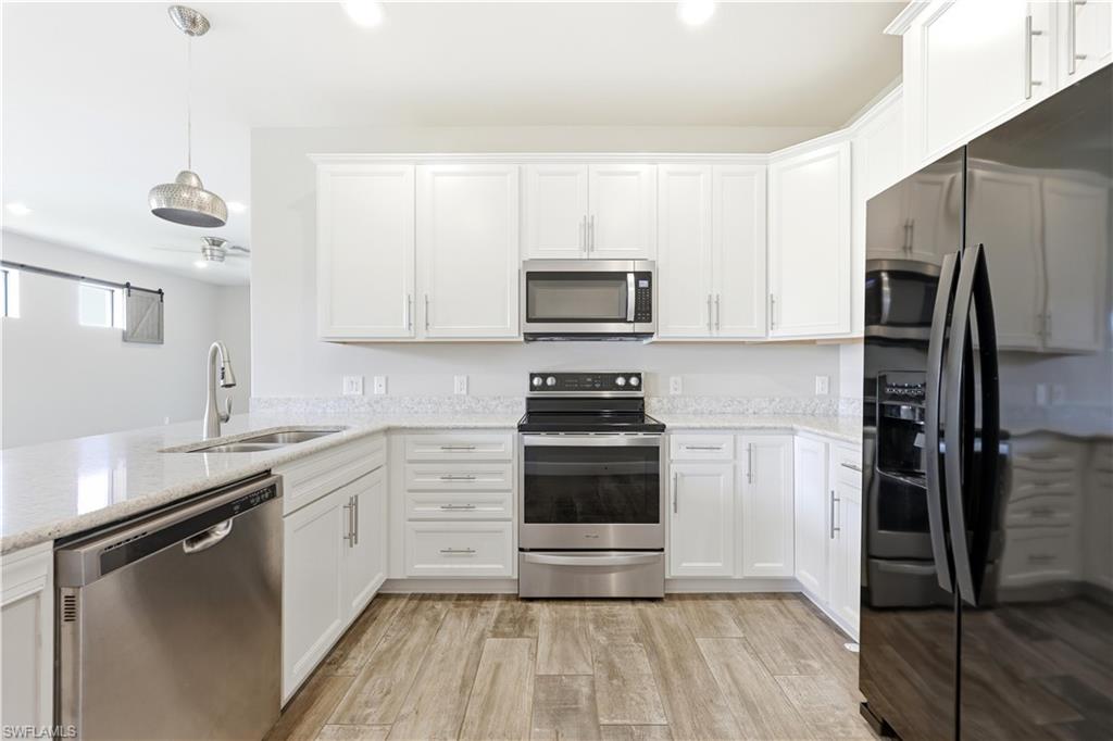 Kitchen featuring white cabinetry, light-toned countertops, stainless steel appliances, and wood-finish flooring