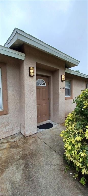 Stucco exterior featuring a recessed entry, arched transom window, and two wall-mounted outdoor sconces