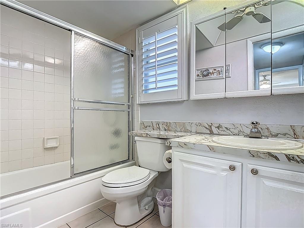 Bathroom with vanity, tile patterned flooring, toilet, and enclosed tub / shower combo