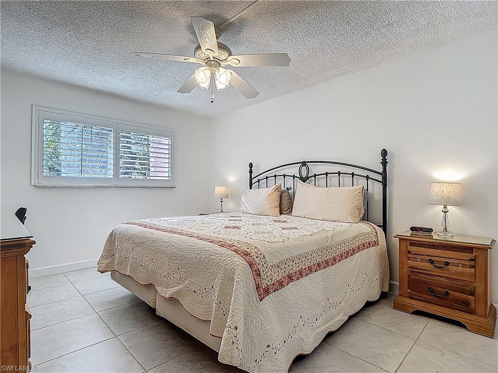 Bedroom with light tile patterned flooring, a textured ceiling, ceiling fan, and baseboards