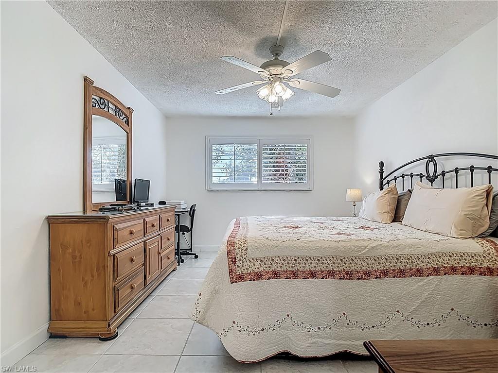 Bedroom with light tile patterned floors, baseboards, a textured ceiling, a ceiling fan, and a desk