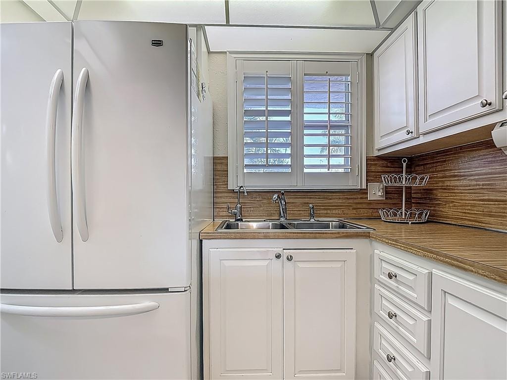 Kitchen with freestanding refrigerator, a sink, white cabinets, and decorative backsplash