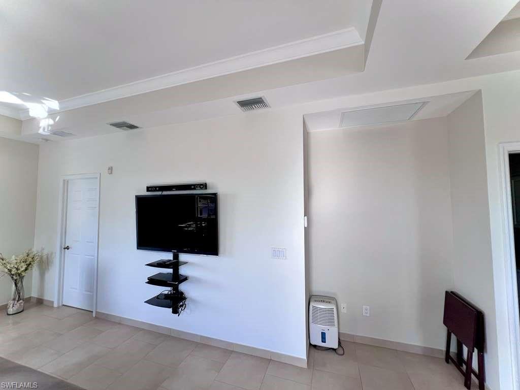 Recessed ceiling with crown molding, tile flooring, and a mounted entertainment shelf unit