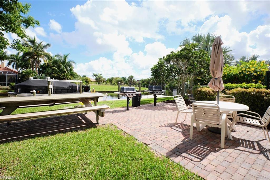 Brick paver patio with a picnic table and additional outdoor seating, bordered by a green lawn and mature landscaping