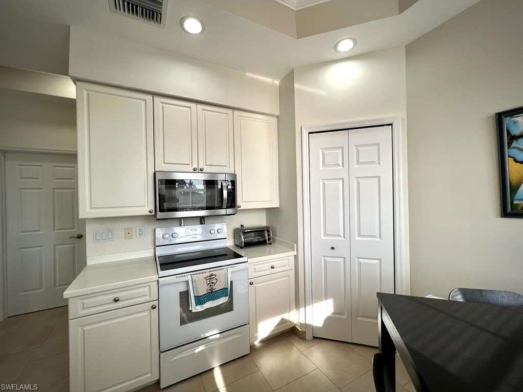Kitchen featuring cream-colored cabinetry with stainless hardware, a white electric range, and a stainless steel over-the-range microwave