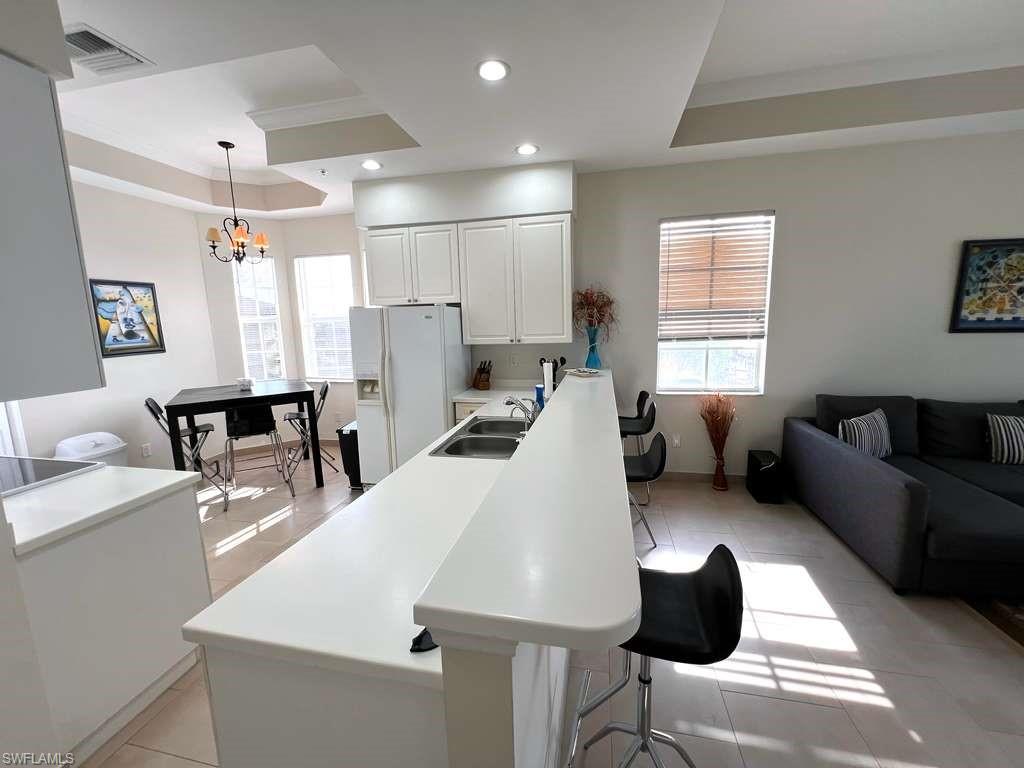 Open-concept living space featuring a kitchen island with seating, recessed lighting, white cabinetry, and tray ceilings