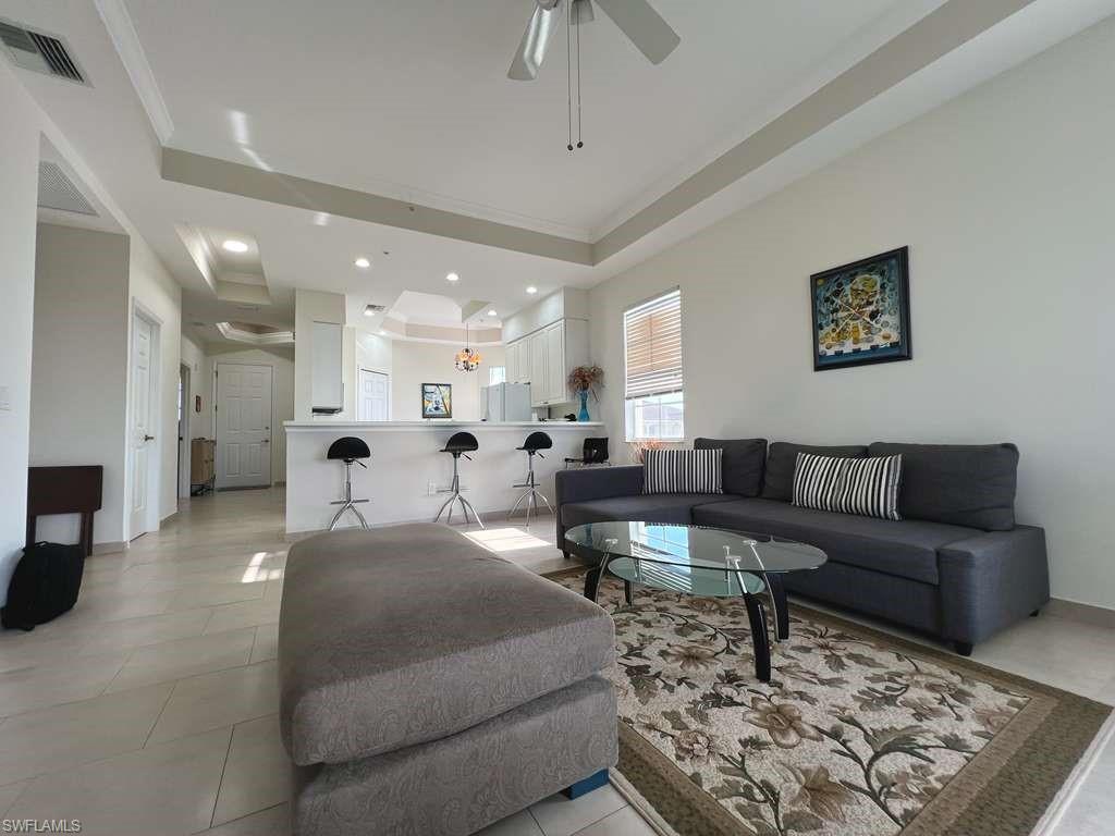 Open-concept living space featuring tray ceilings with recessed lighting, tile flooring, and a kitchen pass-through with breakfast bar
