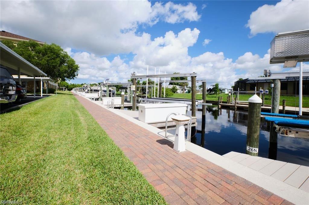 Waterfront property featuring multiple boat slips with lifts, a brick paver walkway, and a manicured lawn