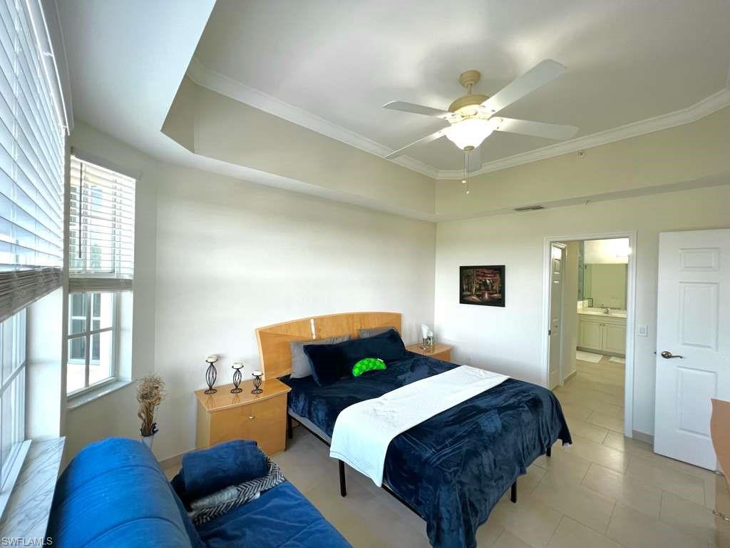 Bedroom featuring a tray ceiling with crown molding, a ceiling fan, and large windows with blinds