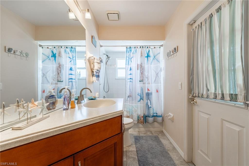 Bathroom featuring a single vanity with a countertop basin, a large wall-mounted mirror, track lighting, and a shower with white tiled walls