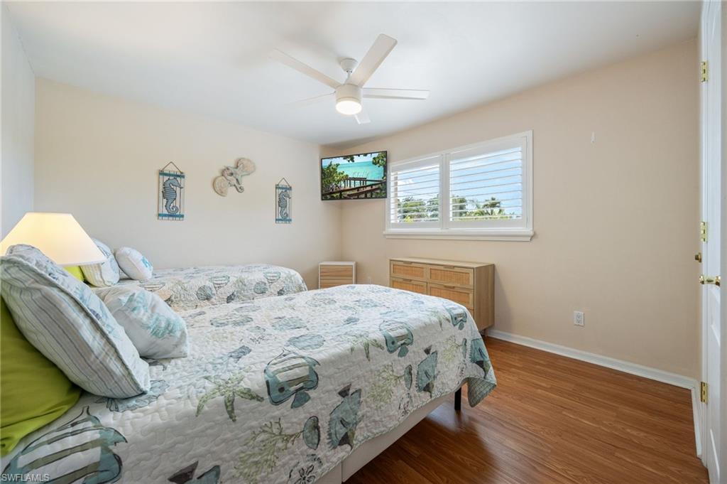 Room featuring wood-finish flooring, a ceiling fan, and a window with white plantation shutters