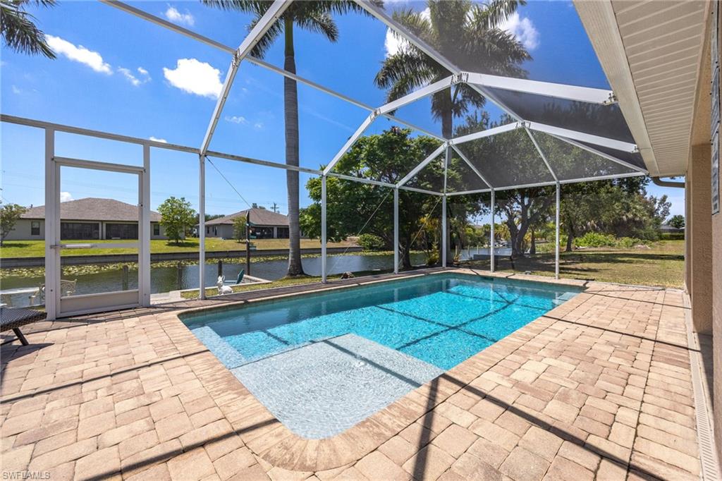 Screened outdoor pool area featuring a rectangular pool with an integrated sun shelf, surrounded by paver decking, and a canal with a dock