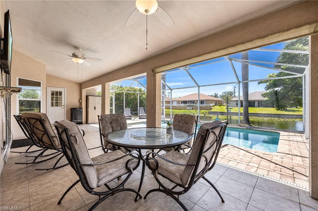 Screened lanai featuring neutral tile flooring, dual ceiling fans, a built-in television shelf, and a screened enclosure overlooking a waterway and pool with paver decking