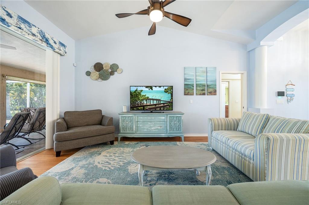 Spacious living area featuring vaulted ceilings, wood-finish flooring, a ceiling fan, and large sliding glass doors leading to an exterior screened patio