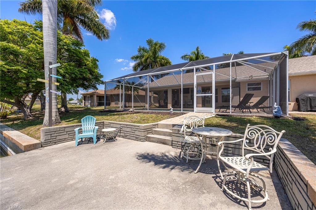 Exterior patio with a block retaining wall, concrete dock, lush landscaping, and a screened enclosure