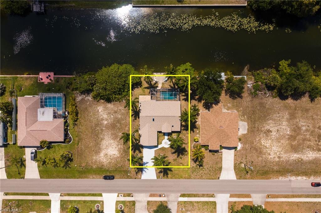 Waterfront property featuring a private swimming pool, mature palm trees, an attached two-car garage, and a concrete driveway