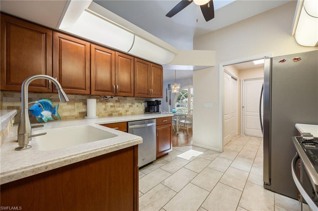 Kitchen featuring rich wood cabinetry, light-toned countertops, a stainless steel sink with a gooseneck faucet, a mosaic tile backsplash, and tile flooring