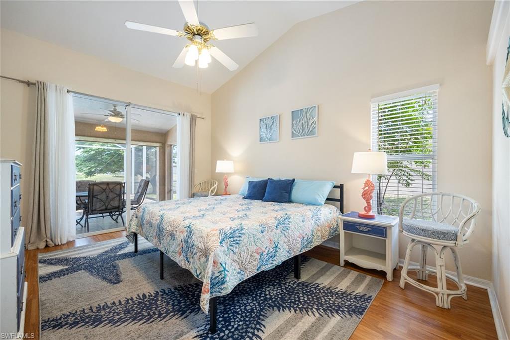 Vaulted ceiling bedroom with wood-finish flooring, featuring a ceiling fan and a sliding glass door leading to a screened lanai with outdoor seating