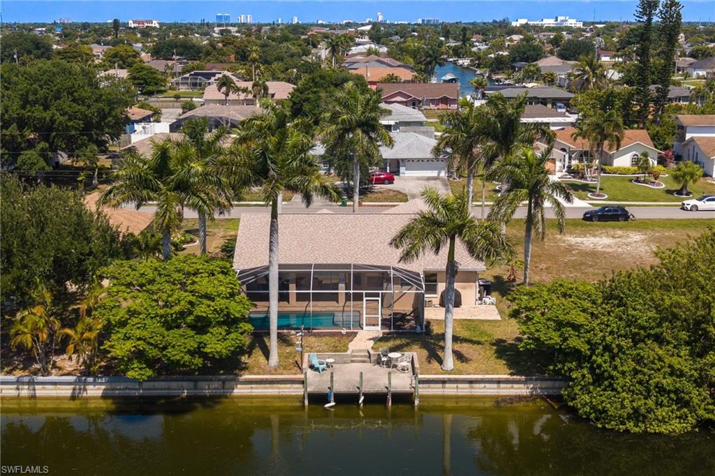 Waterfront residence featuring a private dock, screened pool enclosure, paved patio, and mature palm trees