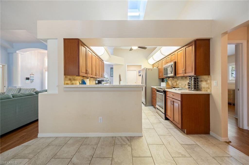 Kitchen featuring warm wood cabinetry, stainless steel appliances, a tiled backsplash, and light-colored countertops