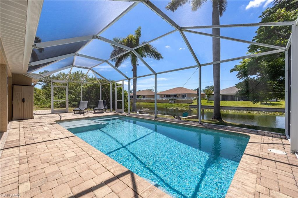 Screened-in swimming pool featuring paver decking, a spa, and water frontage