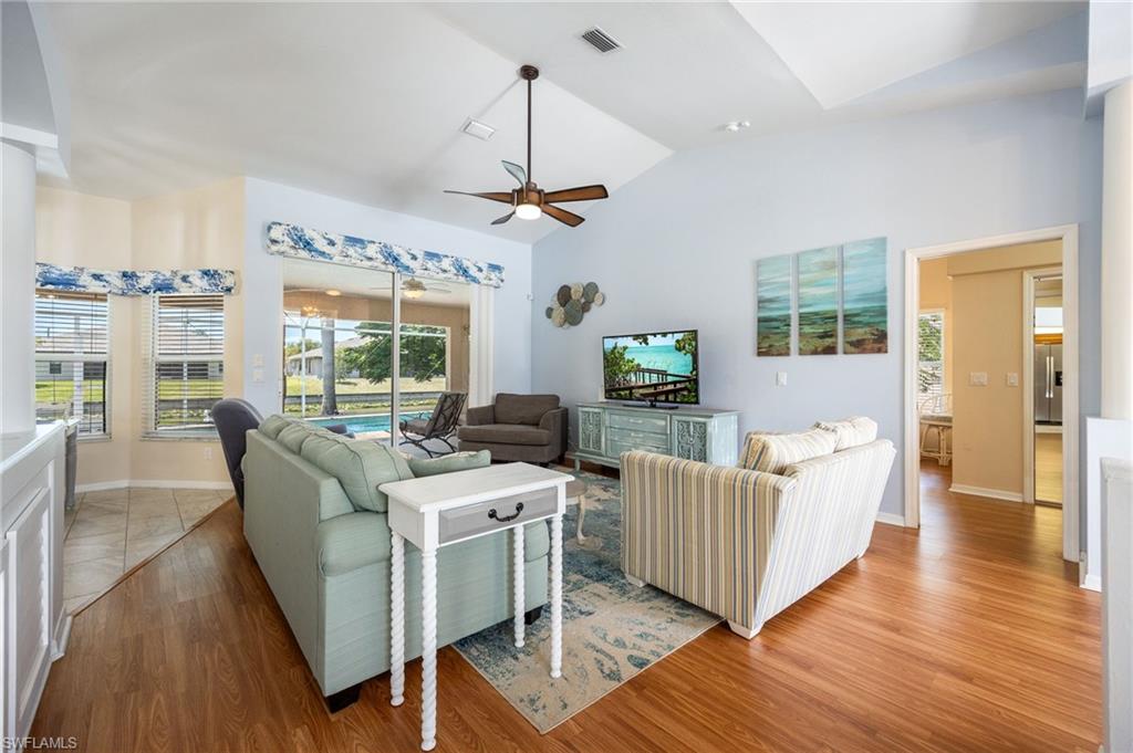 Spacious living area featuring a vaulted ceiling with a ceiling fan, sliding glass doors opening to an outdoor pool, and wood-finish flooring