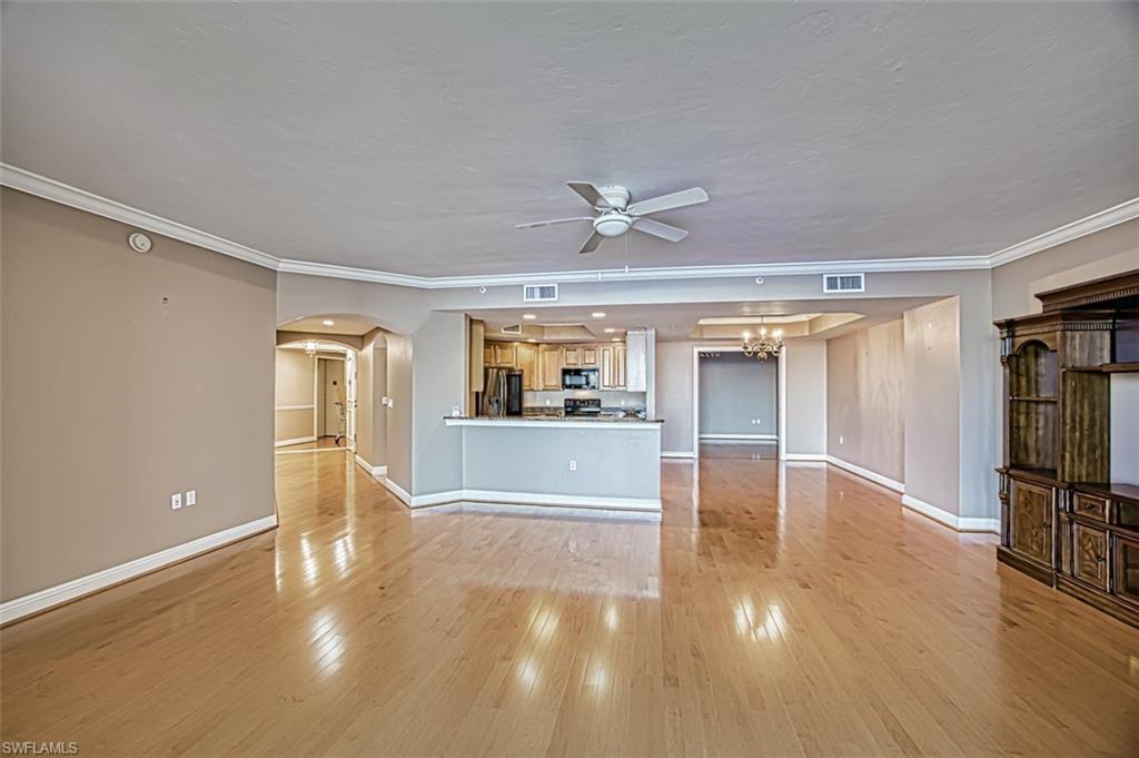 Unfurnished living room with ceiling fan with notable chandelier, light hardwood / wood-style flooring, and crown molding