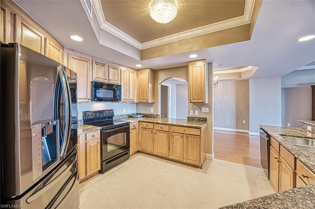 Kitchen with black appliances, a notable chandelier, a raised ceiling, and crown molding