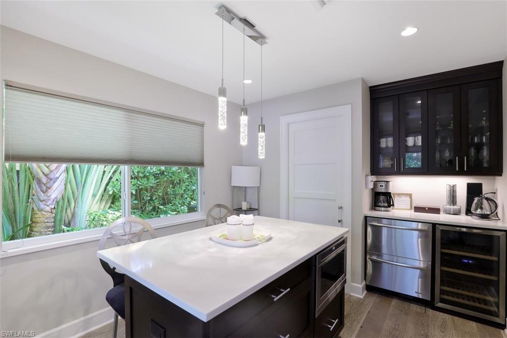 Indoor dry bar with beverage cooler, stainless steel microwave, fridge, dark wood-style flooring, and decorative light fixtures