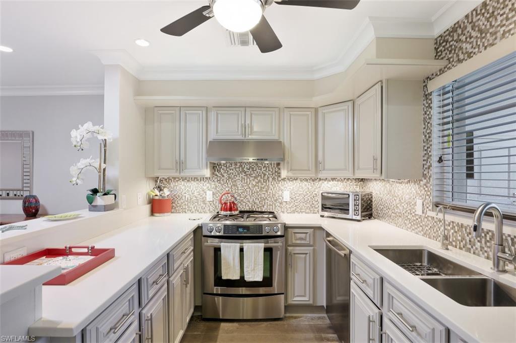 Kitchen with appliances with stainless steel finishes, a sink, under cabinet range hood, ornamental molding, and light countertops