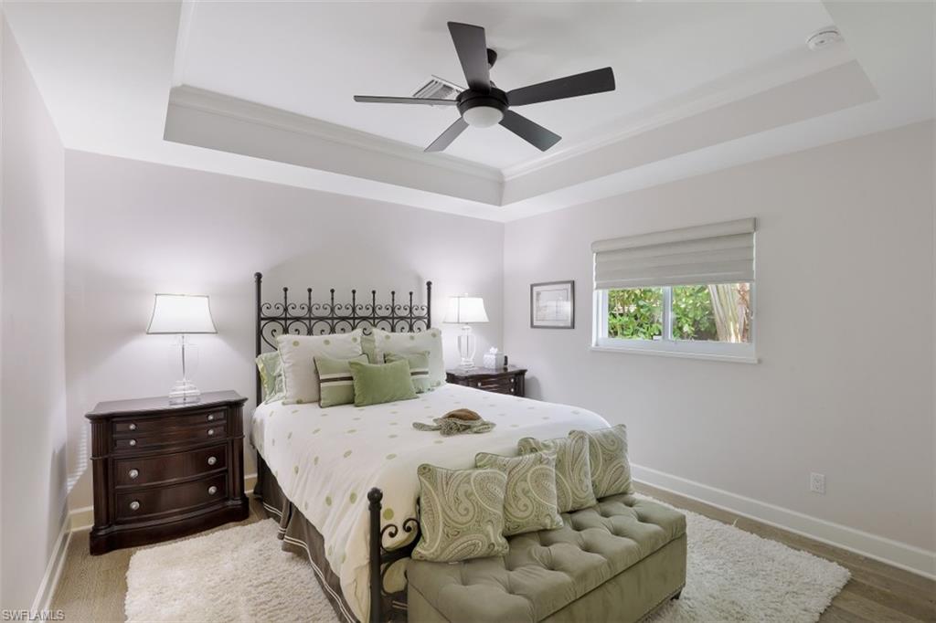 Bedroom featuring a tray ceiling, baseboards, ornamental molding, a ceiling fan, and wood finished floors