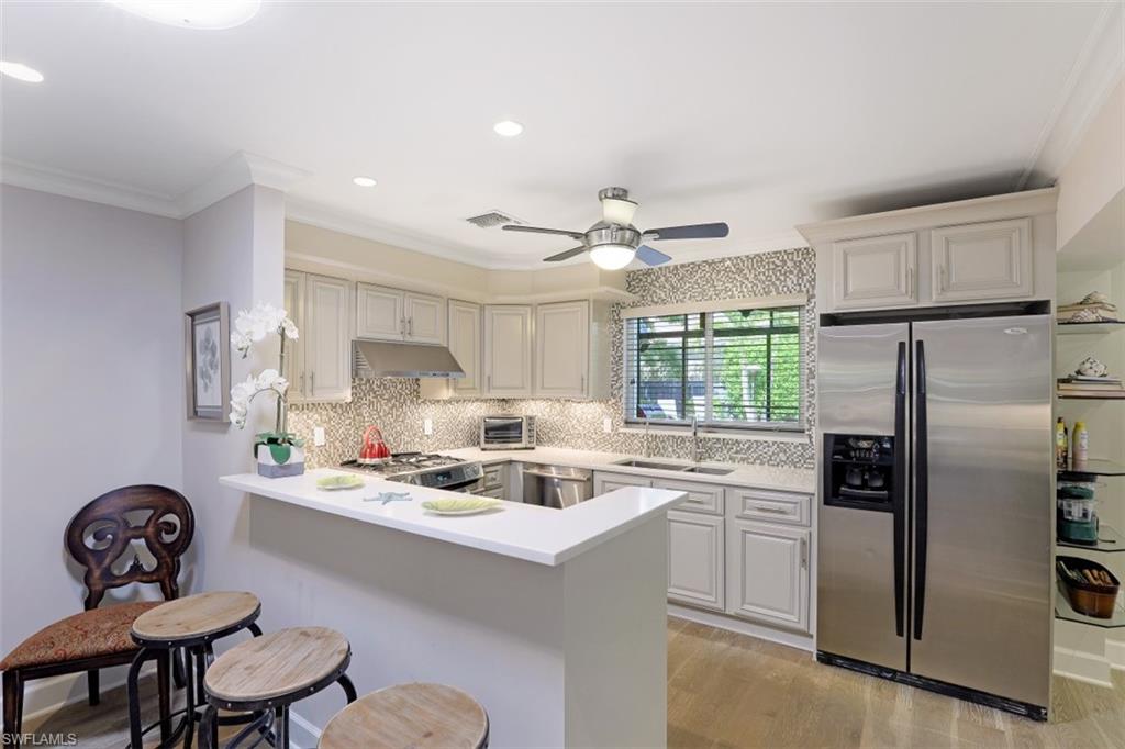 Kitchen featuring appliances with stainless steel finishes, a sink, under cabinet range hood, a kitchen bar, and light countertops